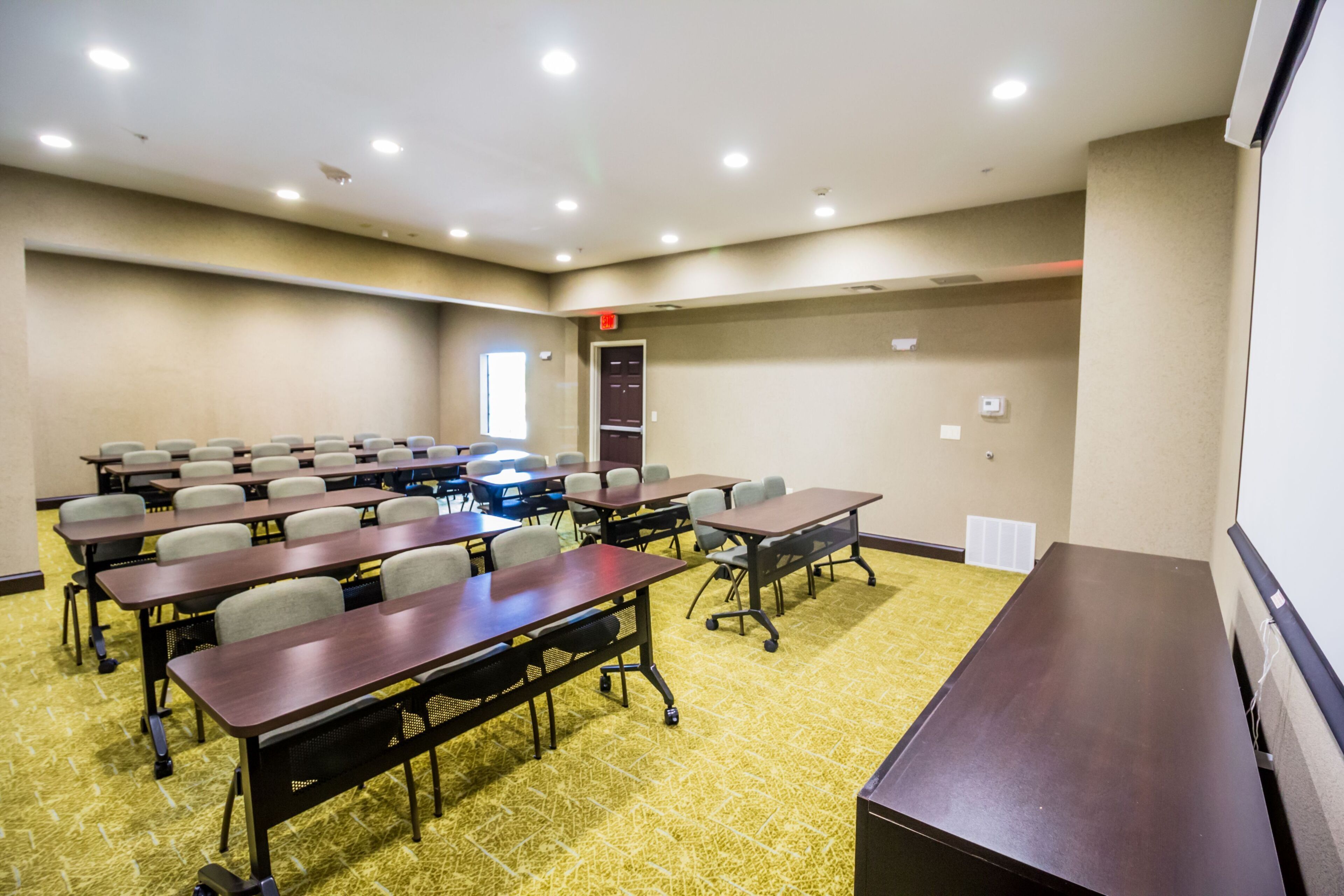 A conference room with multiple tables and chairs, carpeted flooring, and recessed ceiling lights.