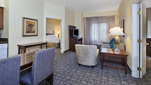 Quarto de hotel com área de refeições, televisão, sofá e luminária.