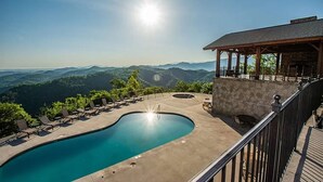 A swimming pool with lounge chairs and a stone wall, overlooking a mountainous landscape. - Endless Views - King Beds - Close to attractions ! (Sevierville)
