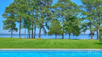 A swimming pool with a clear view of the sea and tall pine trees in the background.