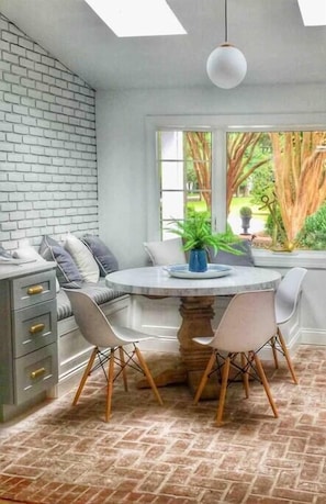 Une cuisine moderne avec un mur en briques, une table de salle à manger ronde accompagnée de deux chaises, et une vue sur la verdure à l’extérieur.