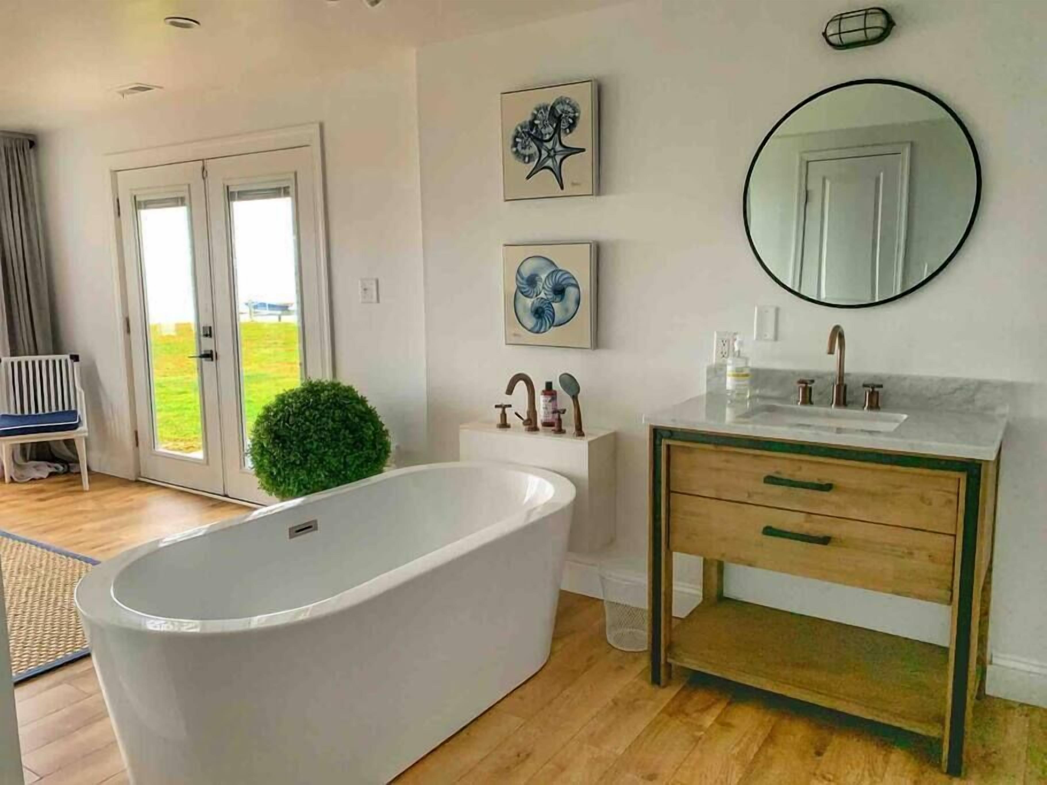 A modern bathroom with a freestanding bathtub, a wooden vanity with a mirror, and two framed artworks on the wall.