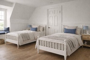 A bedroom with two white beds, a window seat, a door, and a nightstand with a lamp.