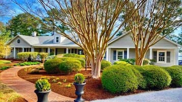 A two-story house with a covered porch and a landscaped garden with trimmed bushes and a paved walkway.