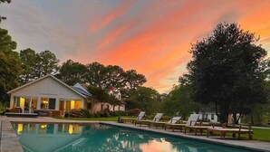 A swimming pool with lounge chairs, a house with a porch, and trees in the background. - Thorneton Point Estate (Easton)