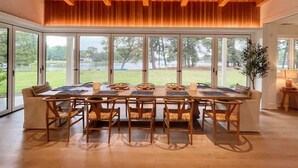 A dining area with a wooden table and chairs, large windows, and a view of the outdoors. - Thorneton Point Estate (Easton)