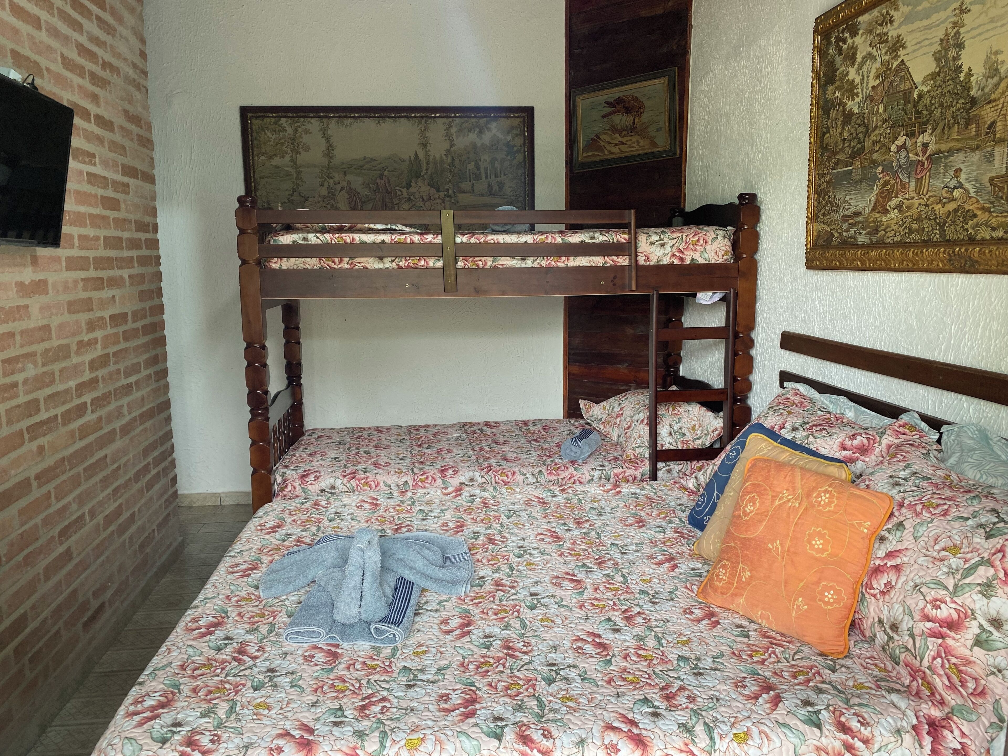A bunk bed with floral bedding, a television on the wall, and artwork on the walls.
