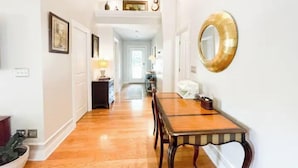 A hallway with a wooden floor, a dining table with chairs, and a round mirror on the wall. - Lovely 3 Bdrm Home w/Free Parking Close to I-75! (Lexington)