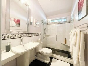 Ein Badezimmer mit weißem Waschbecken, Toilette und Dusche. Ein Handtuchhalter mit einem darüberhängenden Handtuch.
