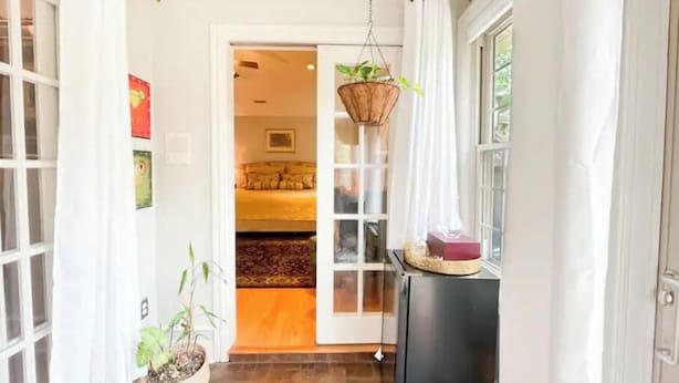 A hallway with a bed in the background, a hanging plant, and a black cabinet. - Lovely 3 Bdrm Home w/Free Parking Close to I-75! (Lexington)