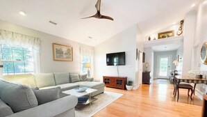 A spacious living room with a grey sofa, wooden flooring, a flat-screen TV, and a dining area with a table and chairs. - Lovely 3 Bdrm Home w/Free Parking Close to I-75! (Lexington)