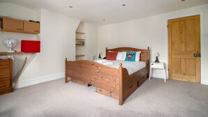 Una camera da letto con un letto di legno, un armadietto rosso, una ventola bianca e una porta in legno.