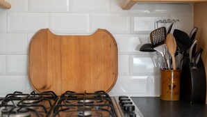 Una cucina con piano cottura a gas, un tagliere in legno e un portautensili con diversi strumenti da cucina.