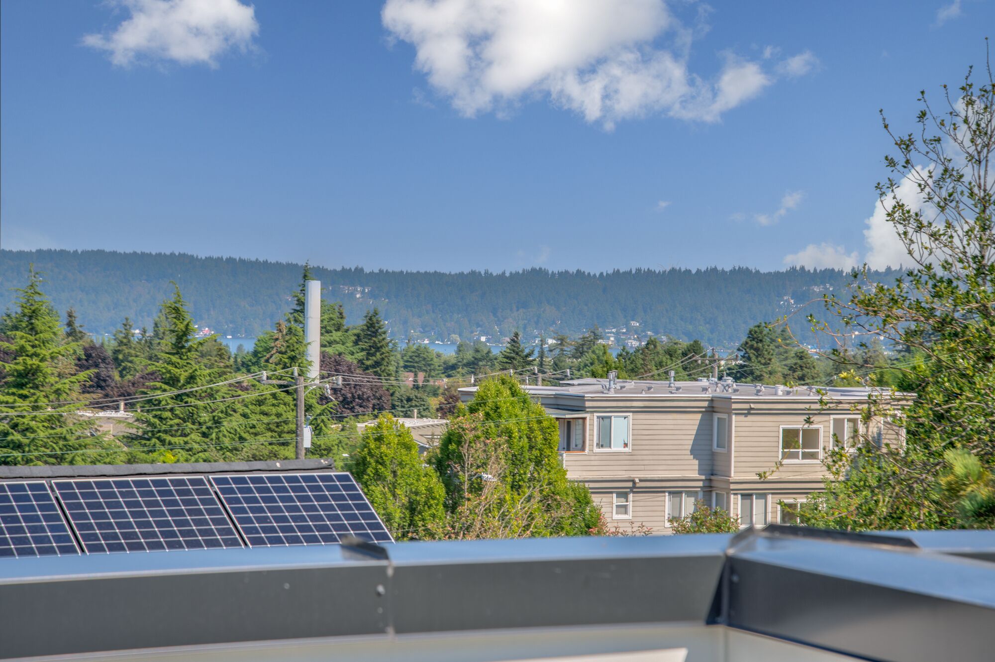 A residential area with houses, solar panels, and a forested hill in the background.