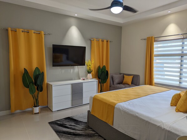A modern bedroom with a bed, a TV, a sofa, and curtains. - Ocho Rios Heights Ultra Lux Villa (Ocho Rios)