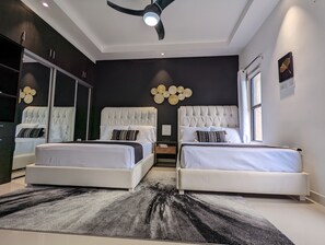 Een moderne slaapkamer met twee bedden, een grote spiegel, een plafondventilator en een decoratief wandobject.