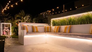 A white outdoor sofa with yellow and white striped cushions, surrounded by greenery and string lights. - Ocho Rios Heights Ultra Lux Villa (Ocho Rios)