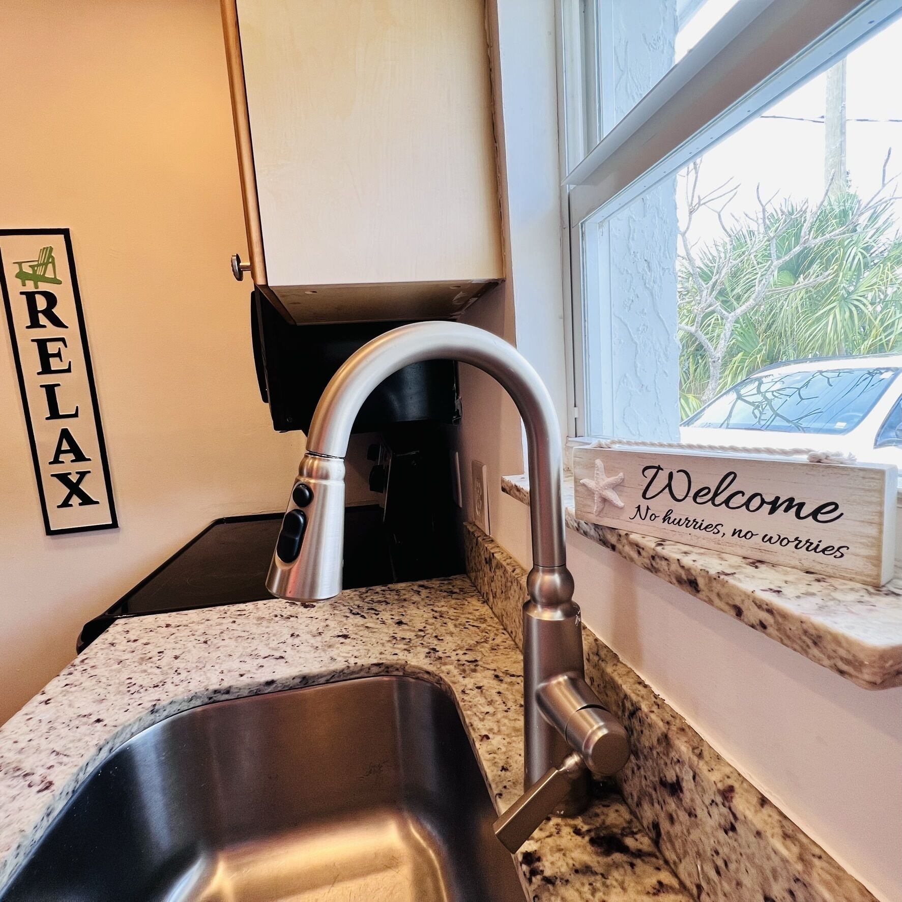 Una cocina con un lavamanos de acero inoxidable, un grifo, un cartel con la palabra 'RELAX' y un cartel de 'Welcome' con una estrella de mar.