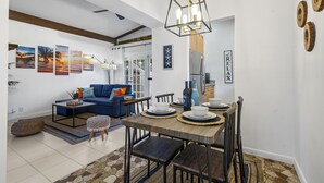 A modern living room with a blue sofa, dining table set with plates and bowls, and a hanging light fixture. - Coco Bay Condos (Fort Lauderdale)