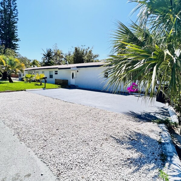 A single-story house with a gravel driveway, surrounded by palm trees and a well-maintained lawn.