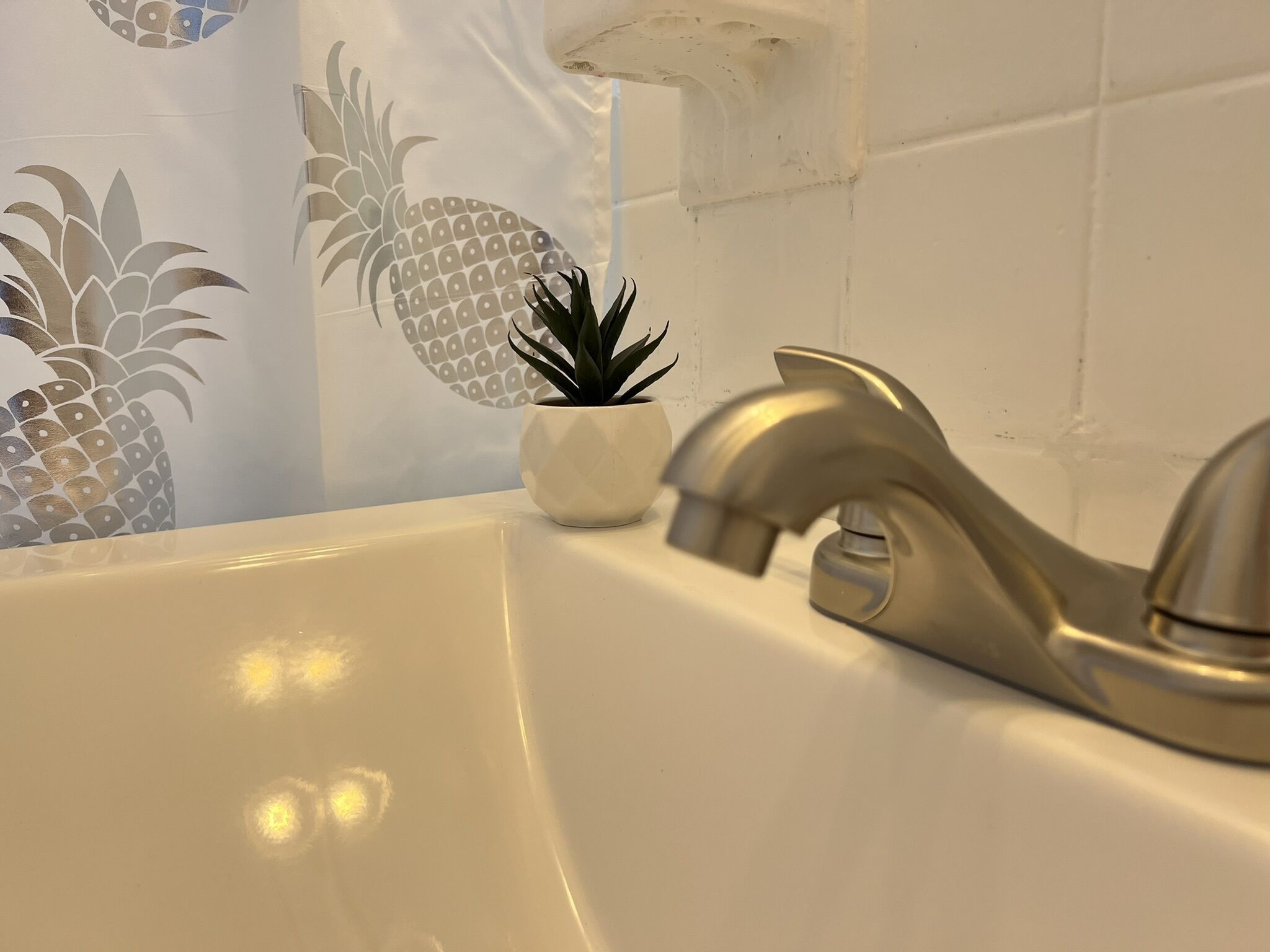 A bathroom with a white sink, a gold faucet, and a pineapple-themed shower curtain.