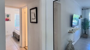 A hallway with a bed, a framed picture, a television, and a potted plant. - Coco Bay Condos (Fort Lauderdale)