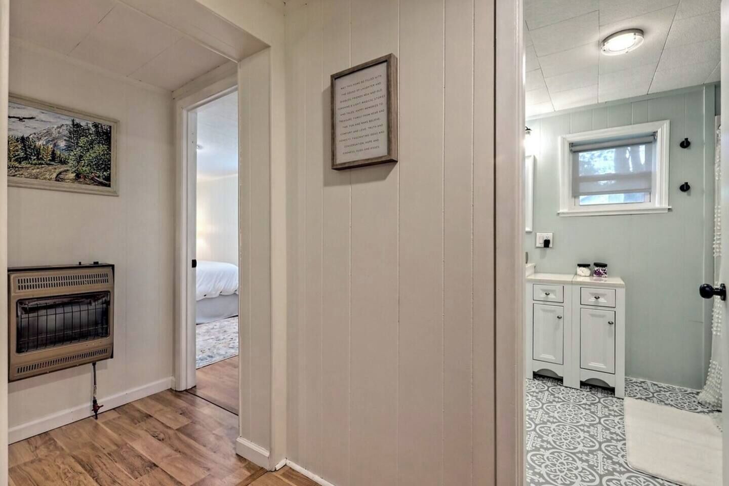 A hallway with a wooden floor, a framed picture on the wall, and a door leading to a bedroom.