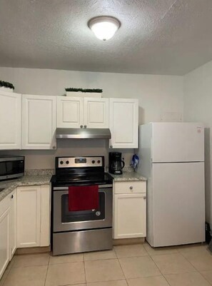 Cocina compacta con armarios blancos, estufa de acero inoxidable, microondas, cafetera y refrigerador blanco.