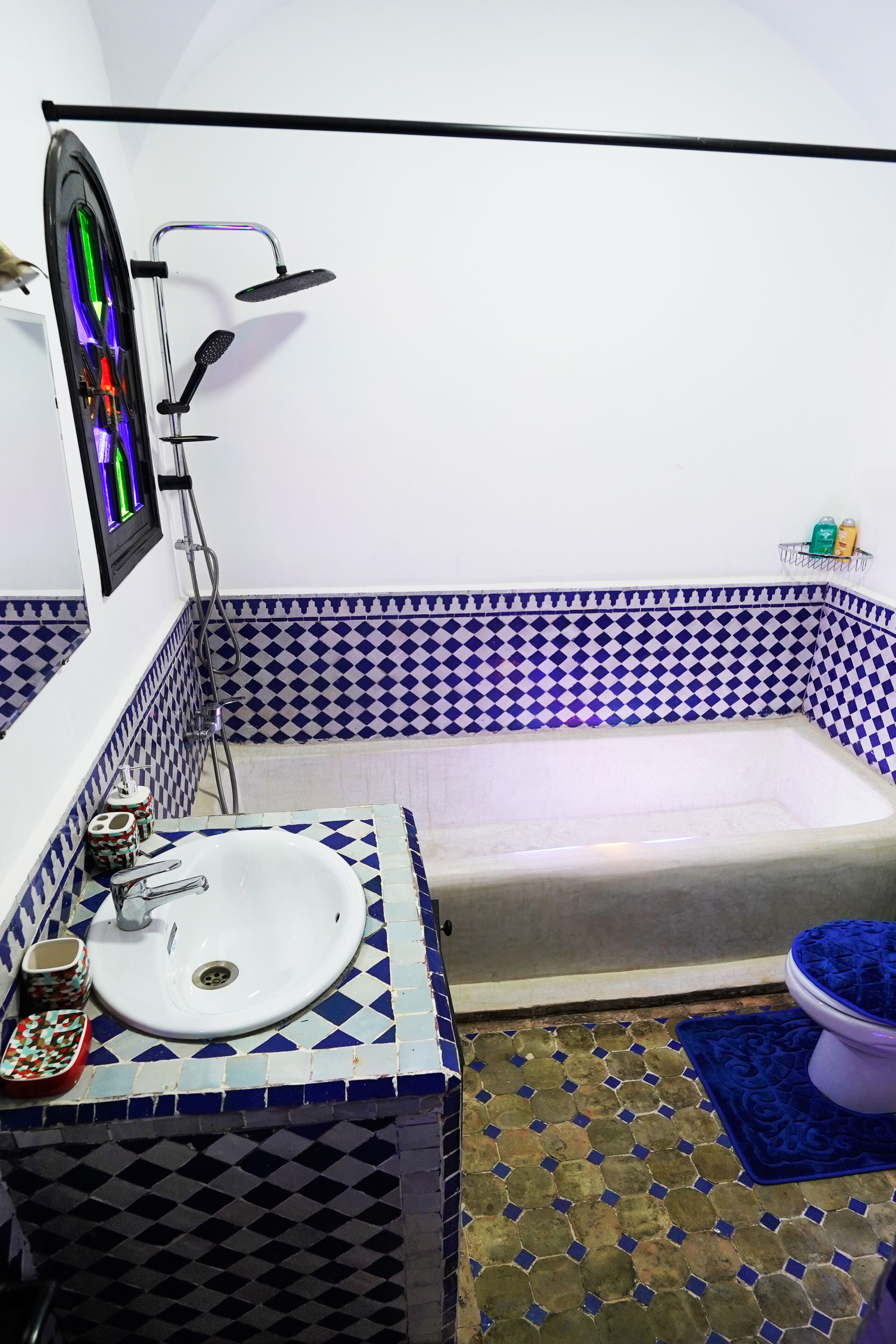 Une salle de bain avec un lavabo blanc, une douche et des toilettes. Les murs sont recouverts de carreaux aux motifs bleus et blancs.