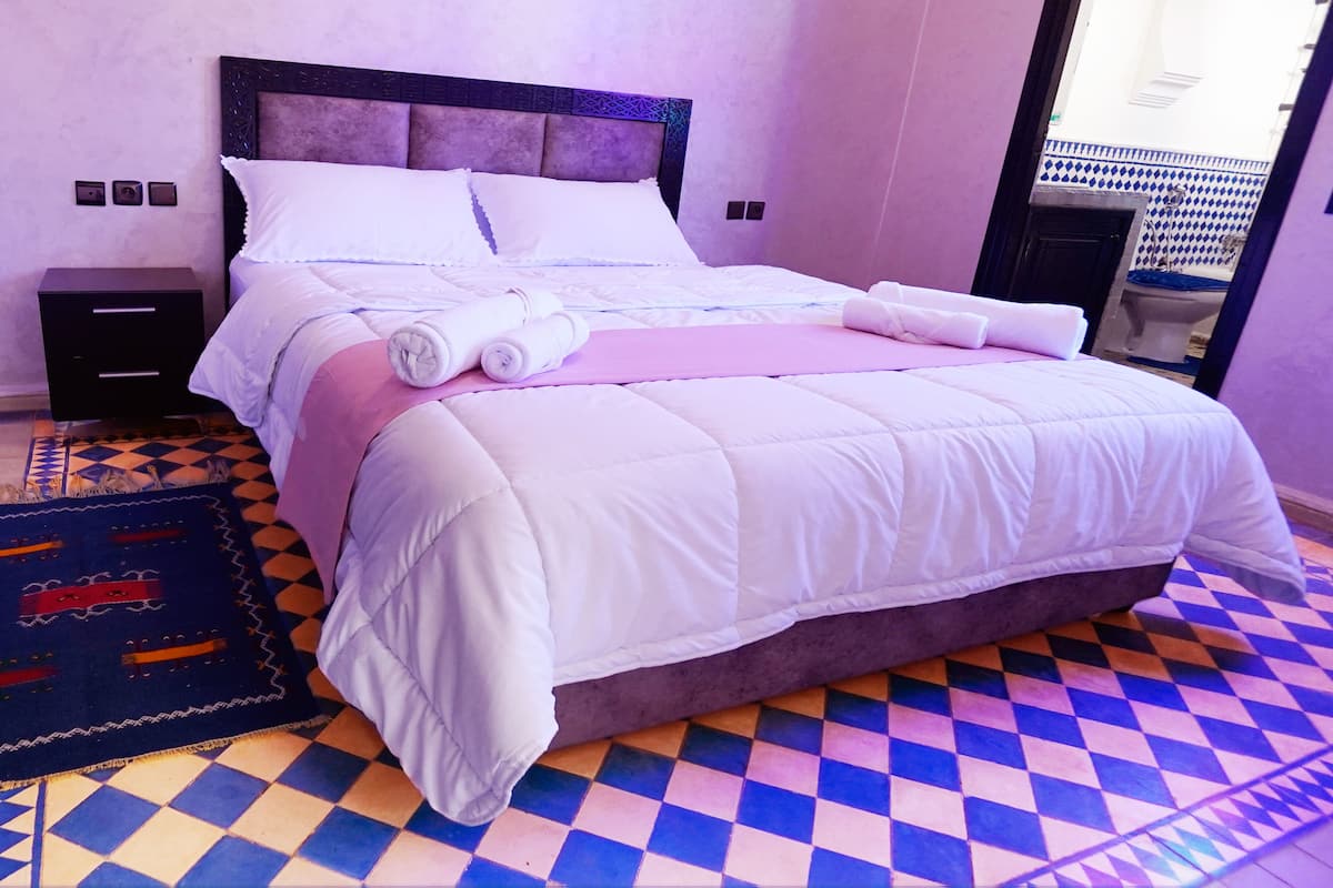A neatly made bed with white linens, a pink blanket, and a headboard with a geometric pattern.