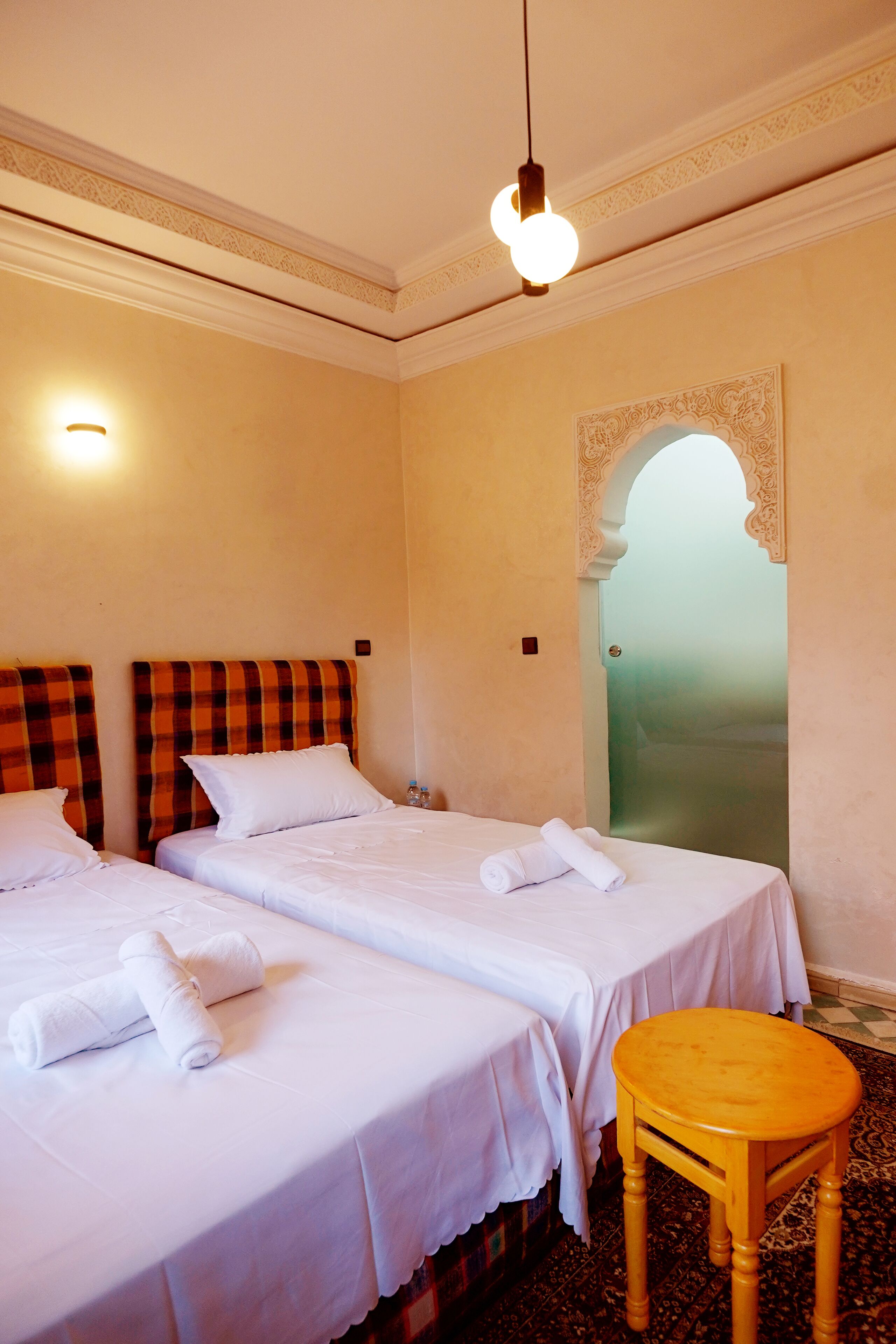 A hotel room with two beds, a small wooden table, and a decorative archway.