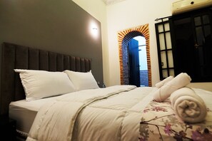 A neatly made bed with white bedding and a floral-patterned blanket, a dark headboard, and a window with a decorative arch. - SOOFSTAY (Marrakech)