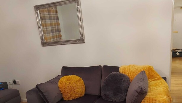 Un salon moderne avec un canapé gris foncé, deux coussins ronds, un plaid jaune et un miroir au mur.