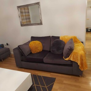 Un salon moderne avec un canapé gris foncé, deux coussins ronds, un plaid jaune et un miroir au mur.
