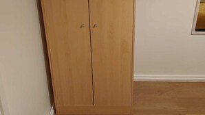 Une armoire en bois à deux portes, avec une petite fenêtre en haut.