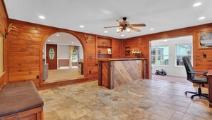 A spacious room with wooden walls, a stone-tiled floor, a ceiling fan, and a large window. - Family Friendly Home w/ Large 1 Acre Backyard & Decks (Peach Bottom)