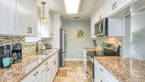 Eine moderne Küche mit weißen Schränken, Granit-Arbeitsplatten, einem Edelstahl-Kühlschrank, einer Mikrowelle und einer Kaffeemaschine.