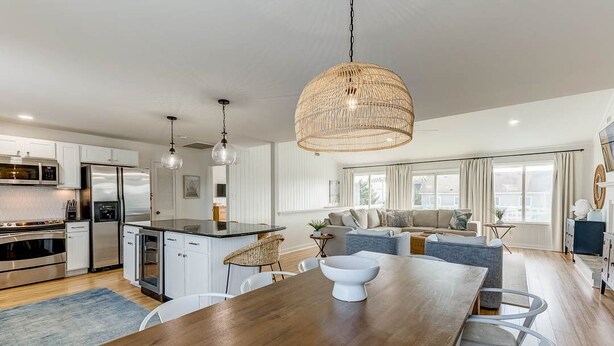 Een moderne keuken met roestvrijstalen apparatuur, een eetgedeelte met een houten tafel, en een woonruimte met een bank en een groot raam.