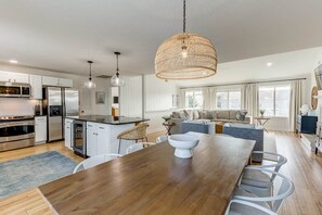 A modern kitchen with stainless steel appliances, a dining area with a wooden table, and a living space with a sofa and a large window. - Gander Getaway | 740 ft to the beach | Private Pool (Virginia Beach)