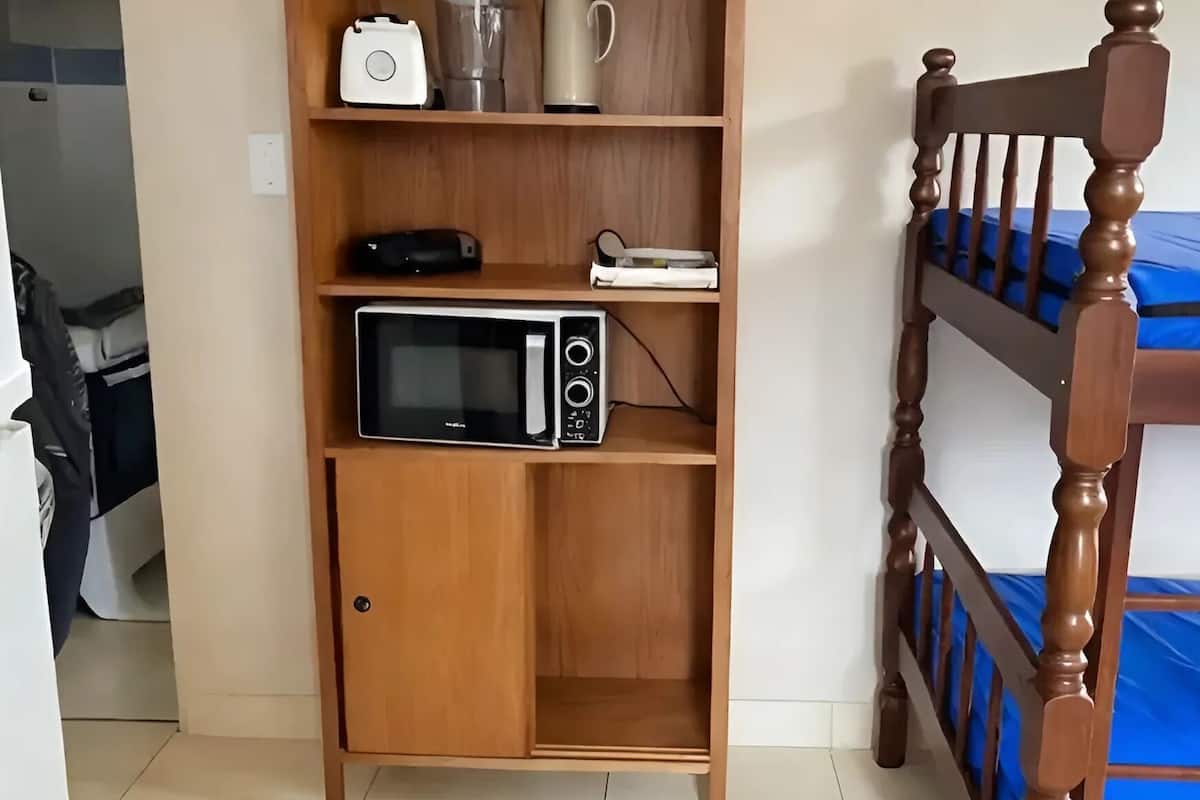 A wooden shelf unit with a microwave, a kettle, and a coffee maker.