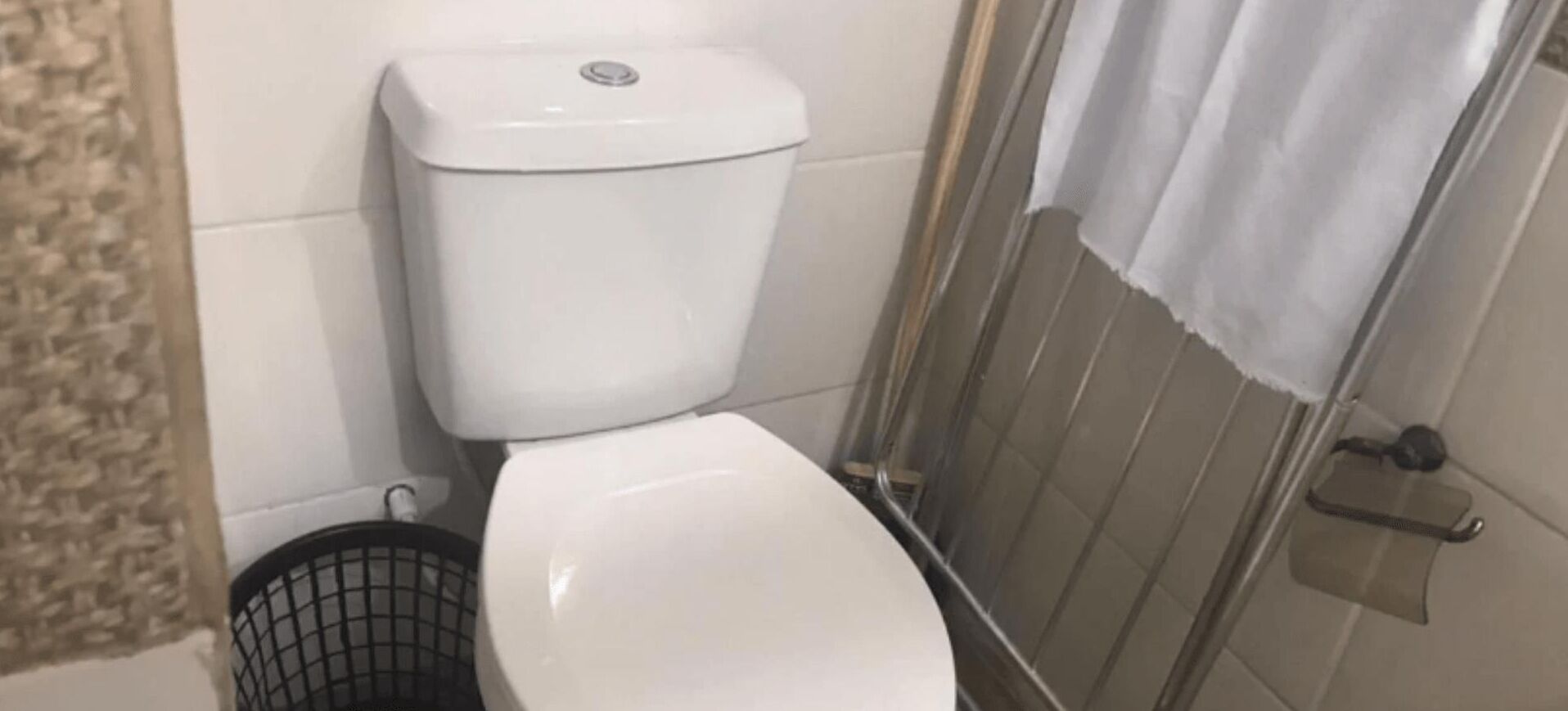 Un baño con inodoro blanco, zona de ducha y pared con azulejos.