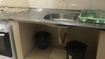 Una cocina con un lavamanos de acero inoxidable, una estufa a gas, un cubo azul y un bote de basura negro.