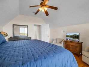 A bedroom with a large bed, a ceiling fan, a dresser, a chair, and a TV.