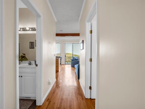A hallway with a wooden floor, white walls, and a door leading to a balcony with a view.