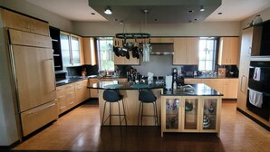 A modern kitchen with wooden cabinets, a central island with stools, and various kitchen appliances.