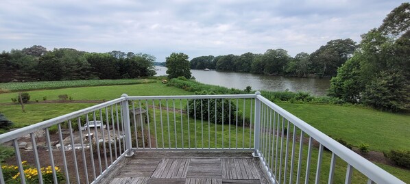 A wooden deck with a white railing overlooking a river, surrounded by lush greenery and trees.