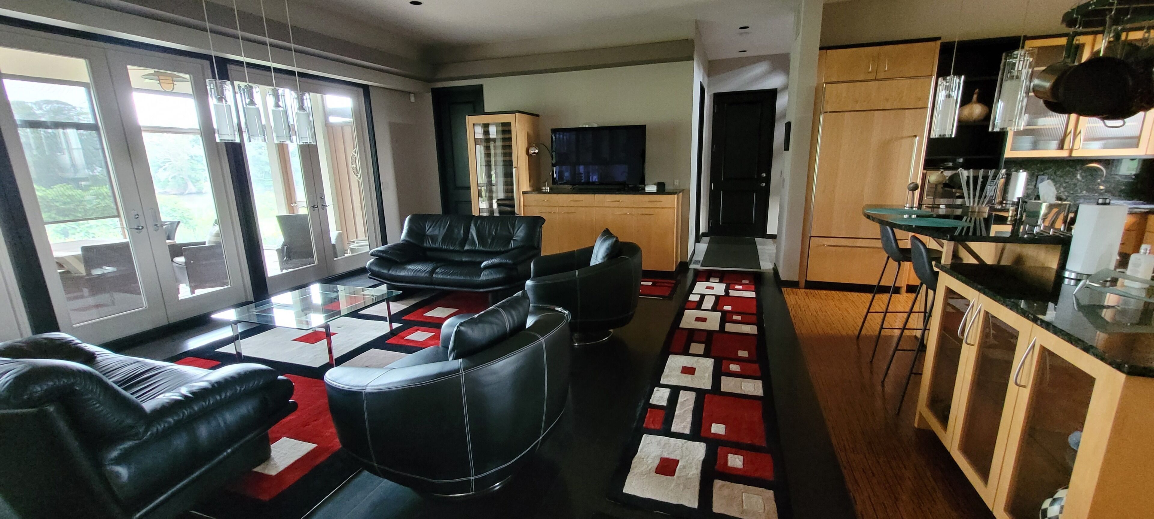 Un salon moderne avec un canapé, un coin repas agrémenté d’un tapis à motifs et une cuisine dotée de meubles en bois et d’un téléviseur.
