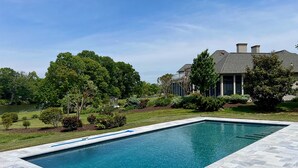 A rectangular swimming pool with a tiled deck, surrounded by a well-maintained lawn and trees.