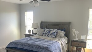 A bedroom with a bed, a ceiling fan, bedside lamps, a nightstand, and a window. - Beautiful home in Sun City! (Sun City)