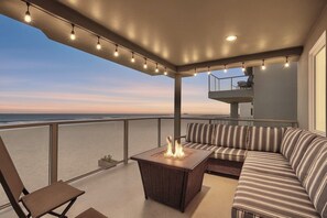 A balcony with a fire pit, seating, and a view of the ocean.